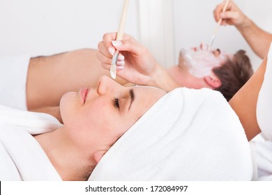 Therapist Applying Facial Mask To Young Couple At Beauty Salon