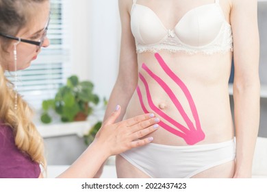 Therapist is applying to stomach kinesio tape. Young woman on taping procedure in spa salon. Tummy tuck with kinesiology