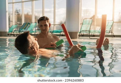 Therapist assisting patient with leg exercises using pool noodles at rehab center - Powered by Shutterstock