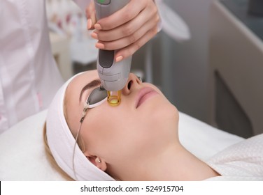 Therapist beautician makes a laser treatment to young woman's face at beauty SPA clinic. Facial laser hair removal epilation procedures. Close up, selective focus.