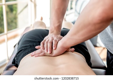 Therapist Giving Lower Back Sports Massage To Athlete Male Patient In Clinic