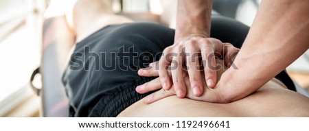 Therapist giving lower back sports massage to athlete male patient in clinic