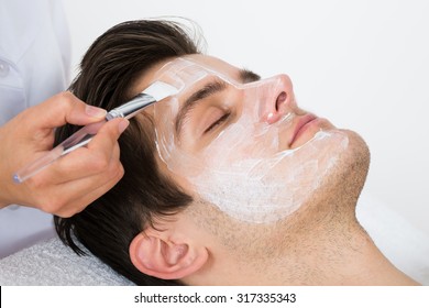 Therapist Hands With Brush Applying Face Mask To A Young Man In A Spa