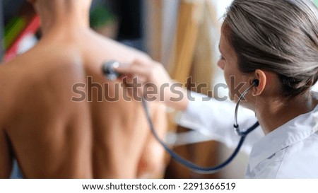 Therapist listens to man breathing using stethoscope. Attentive female doctor examines patient in clinic on blurred background backside view