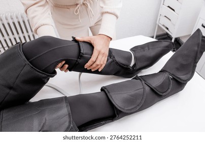 Therapist Operating Pressotherapy Machine While Female Client Lies with Full Leg Air Compression Boots on Massage Table — Professional Pneumatic Lymphatic Drainage Treatment for Legs, Anti-Cellulite Body Contouring, Circulation Therapy and Modern Aesthetic Medicine Spa Concept