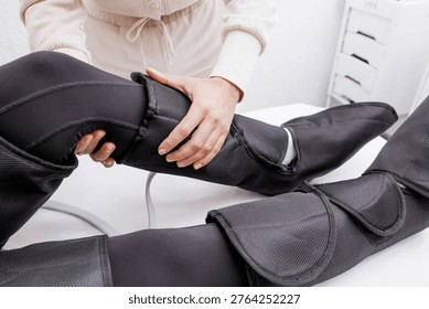 Therapist Operating Pressotherapy Machine While Female Client Lies with Full Leg Air Compression Boots on Massage Table — Professional Pneumatic Lymphatic Drainage Treatment for Legs, Anti-Cellulite Body Contouring, Circulation Therapy and Modern Aesthetic Medicine Spa Concept