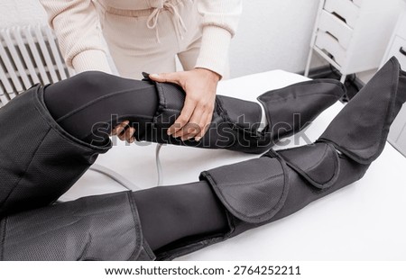 Therapist Operating Pressotherapy Machine While Female Client Lies with Full Leg Air Compression Boots on Massage Table — Professional Pneumatic Lymphatic Drainage Treatment for Legs, Anti-Cellulite Body Contouring, Circulation Therapy and Modern Aesthetic Medicine Spa Concept