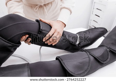 Therapist Operating Pressotherapy Machine While Female Client Lies with Full Leg Air Compression Boots on Massage Table — Professional Pneumatic Lymphatic Drainage Treatment for Legs, Anti-Cellulite Body Contouring, Circulation Therapy and Modern Aesthetic Medicine Spa Concept