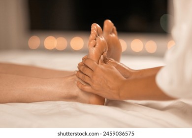 A therapist is performing a relaxing foot massage on a client who is lying down, set against a backdrop of soft, warm ambient lighting that suggests an evening atmosphere designed for relaxation - Powered by Shutterstock