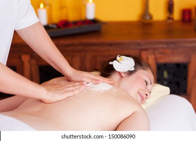 Therapist in a spa cleansing the skin of a beautiful with a salt treatment to exfoliate dead cells and energise with marine minerals