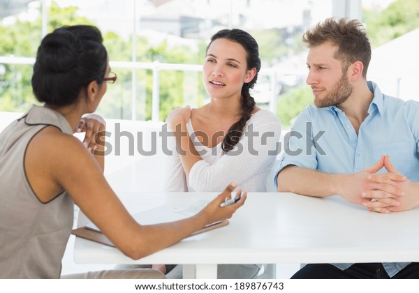 Therapist talking with couple sitting at desk in\
therapists office