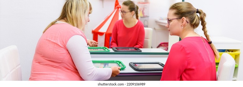 Therapist Teaching Young Mother Of A Non-verbal Child How To Use Speech-generating Device. Augmentative And Alternative Communication AAC Device.