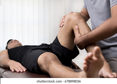 Therapist treating injured knee of athlete male patient in clinic - sport physical therapy concept