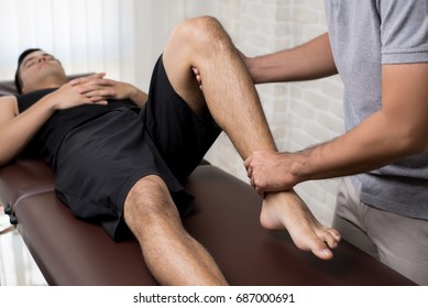 Therapist treating injured leg of athlete male patient in clinic - sport physical therapy concept