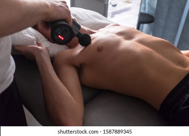 Therapist Treating Injury Of Professional Athlete Male Patient. Black Massage Gun, Used By Professionals To Massage The Body.Sport Physical Therapy Concept. - Photography