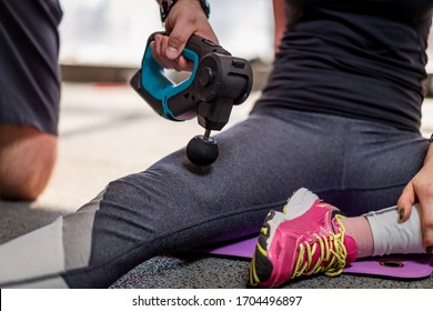 Therapist Treating Injury Of Professional Athlete Female Patient. Black Massage Gun, Used By Professionals To Massage The Body. Sport Physical Therapy Concept