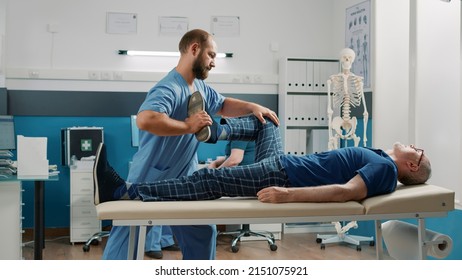 Therapist Using Legs Raise Exercise To Stretch Muscles And Crack Bones, Helping Senior Man With Mechanical Disorders In Cabinet. Male Osteopath Doing Alternative Medicine Procedure.