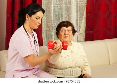 Therapist Woman Helping Senior To Do Exercises With Barbell Home