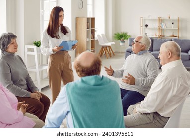 Therapy for seniors. Elderly people attend group therapy session in nursing home and talk to professional psychologist. Mature men and women sit in circle and talk to young woman holding clipboard. - Powered by Shutterstock