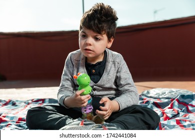 There Is A 5-year-old Boy Playing On The Terrace Of A House With A Plastic, Rattle-like, Green Worm-like Toy. The Child Suffers From Physical And Intellectual Disabilities.