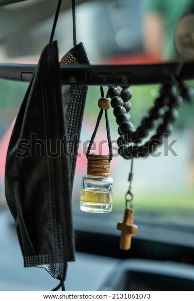 there is a black\
face mask and a perfume bottle next to the car mirror, next to\
which is a small wooden\
cross