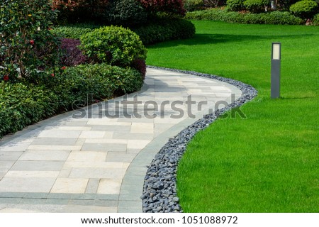 There is a black stone garden on the edge of the curved path, and the landscape lamp is on the green lawn. 