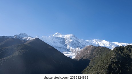 There is a clear sky, a majestic mountain situated between two graceful hills ,View from khangsar, a peaceful village in manang district of Nepal.