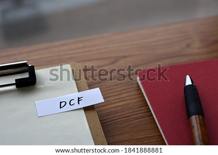There is a clipborad, a pen, and a notebook with a sticky note stuck to it that says DCF written on it. It was an abbreviation for discounted cash flow.