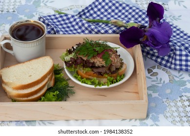 There Is A Cup Of Coffee On A Wooden Tray And A Sandwich With Salad And Cutlet On A Plate. Nearby Are Pieces Of Bread With Lettuce Leaves. Next To The Tray Is A Blue Napkin And A Dark Blue Iris. 