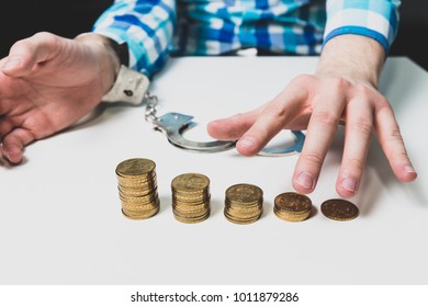 There are gold coins on the table, the man freed himself from the cuffs and reaches for the coins. Machle financial, financial problems, financial pyramid. Criminal liability for financial crimes.