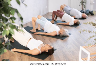 There is group Pilates class in studio for people of different ages. Elderly woman in company of hatha yoga lovers performs bridge pose, setu bandha sarvangasana - Powered by Shutterstock