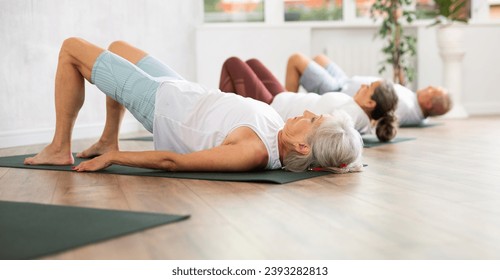 There is group Pilates class in studio for people of different ages. Elderly woman in company of hatha yoga lovers performs bridge pose, setu bandha sarvangasana - Powered by Shutterstock