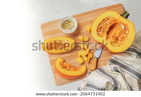 There is a half pumpkin and two cut pieces on a wooden board. Top view of the vegetable