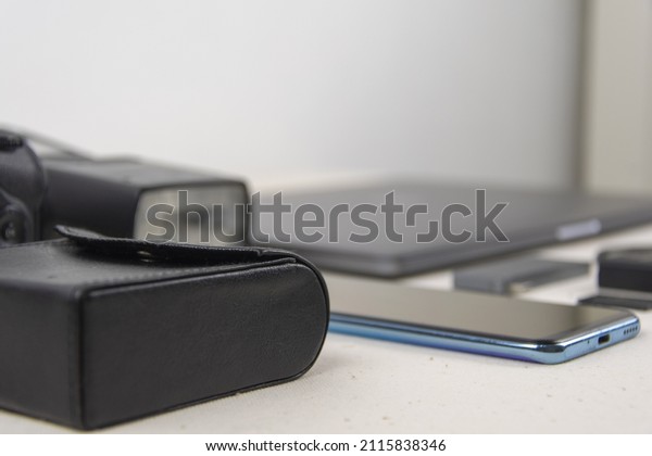 There is a laptop, a\
phone, a camera, a lens, a memory card, light filters for the lens,\
a battery for the camera, a case for filters, an adapter for type-s\
on the table