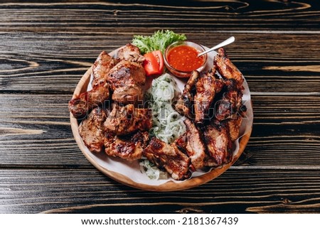 There is a large dish on the wooden table in the new restaurant of the town. There are a lot of meat, a slices of tomato, onion and a red sauce.We can see a leaf near the slices of tomato on the plat