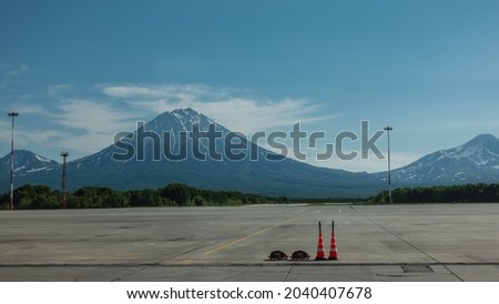 There is a marking on the runway of the airfield. Majestic conical volcanoes with snow-covered slopes rise against the blue sky. Petropavlovsk-Kamchatsky. 