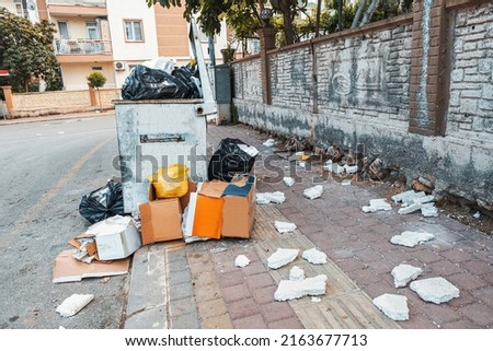 There is a mess and garbage everywhere on the street near trash container bin. Municipal cleaning an ecology
