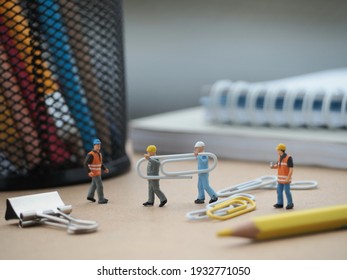 There is miniature toys and paper clip on the table with blurred book and stationery stuff as a backgorund. Office and worker business concept.