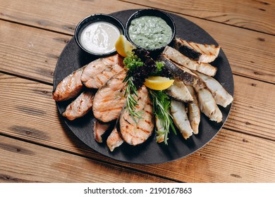 There Is A New Dish With Sauce And Cream In Front Of The Person In The Restaurant. It Looks Very Steamy And Delicious. We Can See A Lot Slices Of Fish And A Slice Of Lemon On The Plate.