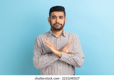 There Is No Way. Concerned Businessman Crossing Hands Showing X Gesture, Rejecting Bullying And Abuse Seriously Looking At Camera, Wearing Striped Shirt. Indoor Studio Shot Isolated On Blue Background