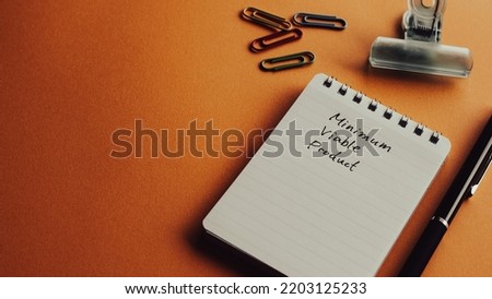 There is a notebook with the word Minimum Viable Product. It's placed on a color background.