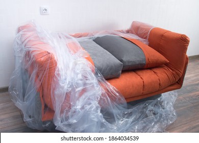 There Is An Orange Sofa In The Room, Partially Covered With Plastic Wrap To Protect It From Dirt And Dust