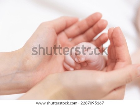 There is mother’s palm on the background of white cloth and the asian korean newborn baby has her hands on it. There is a large empty blank space to use as a copyspace.