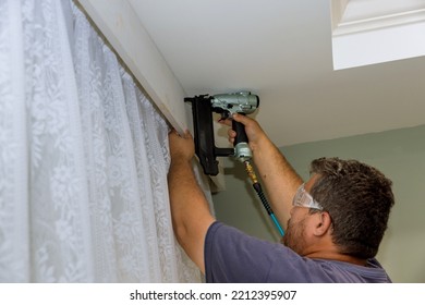 There Is Professional Handyman Who Is Nailing Wooden Cornices On The Curtain Wall Over Window Of A Newly Constructed Home