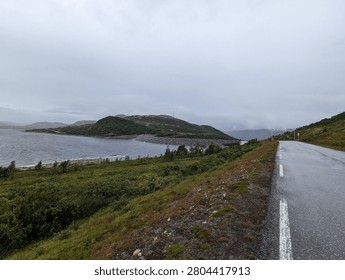 There is a road going down the hill with a body of water in the distance