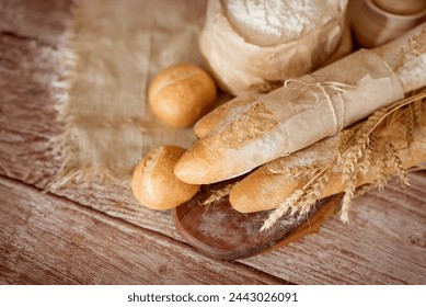 Hay varias baguettes frescas y pequeños rollos en la mesa entre el trigo y la harina. productos de panadería para hornear. pan y rollos en la panadería.