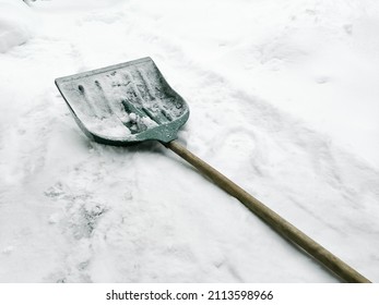 There is a shovel on the snow for snow removal. Green plastic shovel for snow removal. Yard cleaning in winter.