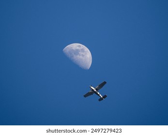 there is a small plane flying in the sky with a half moon in the background