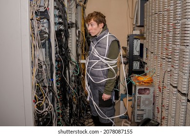 There Is A Technician Wrapped In Wires In The Server Room. A Lot Of Wires Are In The Racks Of The Old Data Center