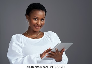 There Are Tons Of Fast And Easy Ways To Make Money Online. Shot Of A Young Woman Using A Digital Tablet While Standing Against A Grey Background.